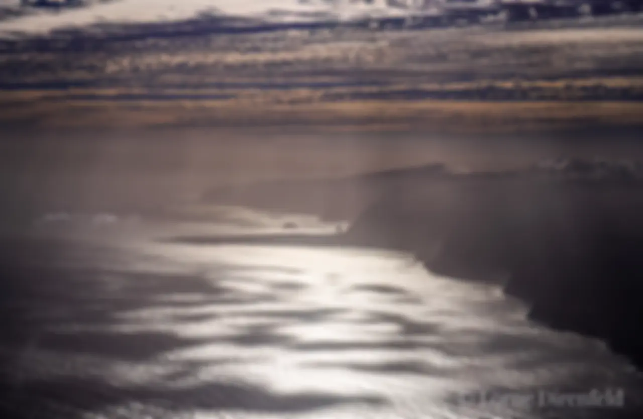 Rays of light pierce the clouds along the north shore of Molokai, with the Kalaupapa peninsula on a misty morning . . .